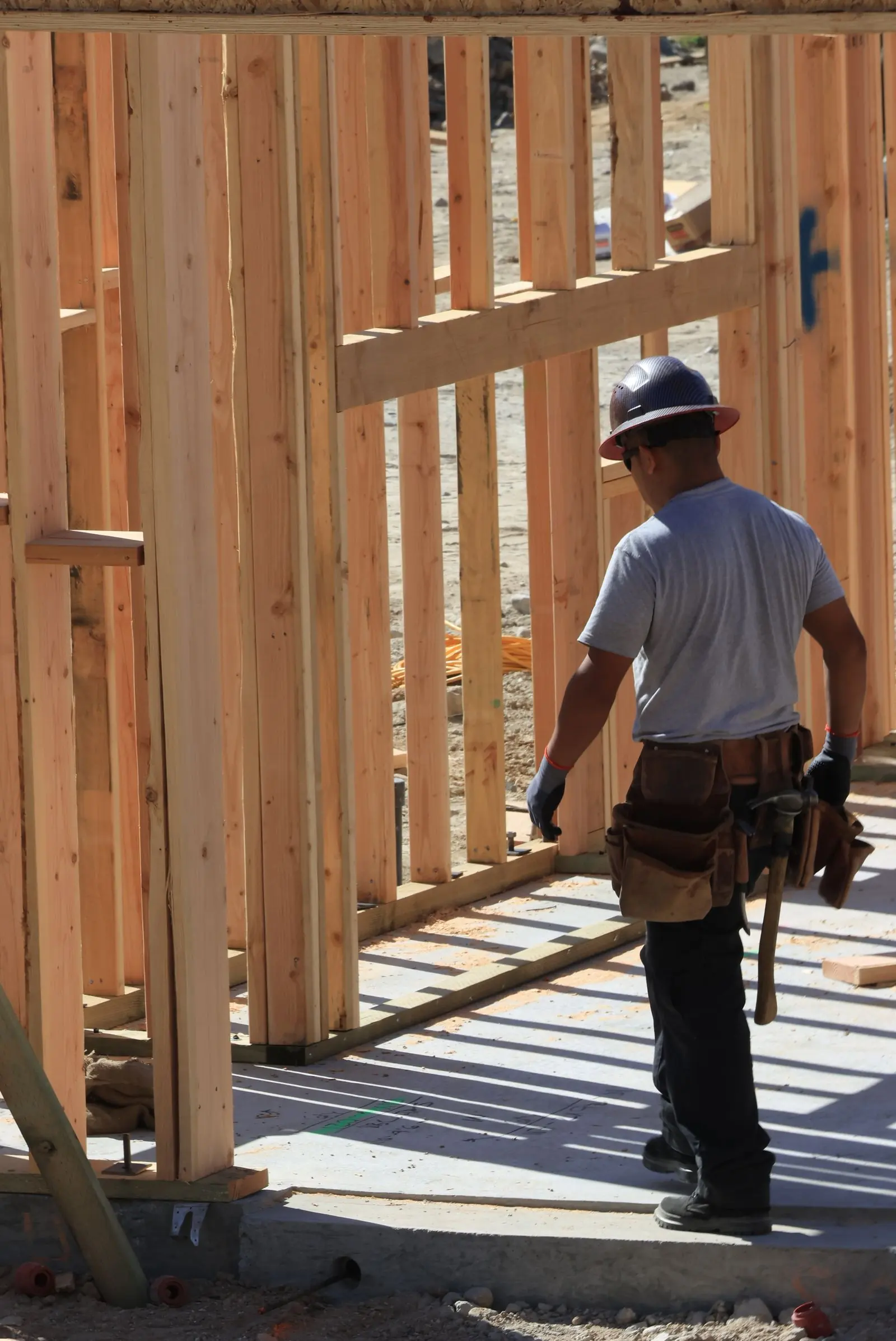 Trabajador de la construcción con cinturón de herramientas revisando el armazón de una vivienda en obra.