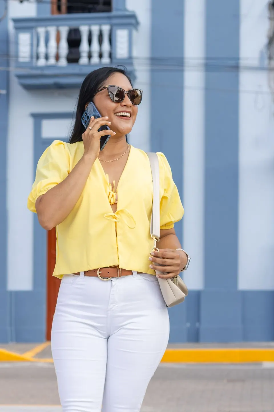 Mujer sonriendo mientras habla por teléfono en una calle de fachadas coloridas.
