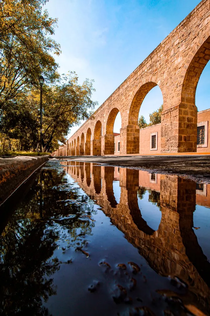 Acueducto histórico de cantera rosa de Morelia, con reflejo en un charco de agua.