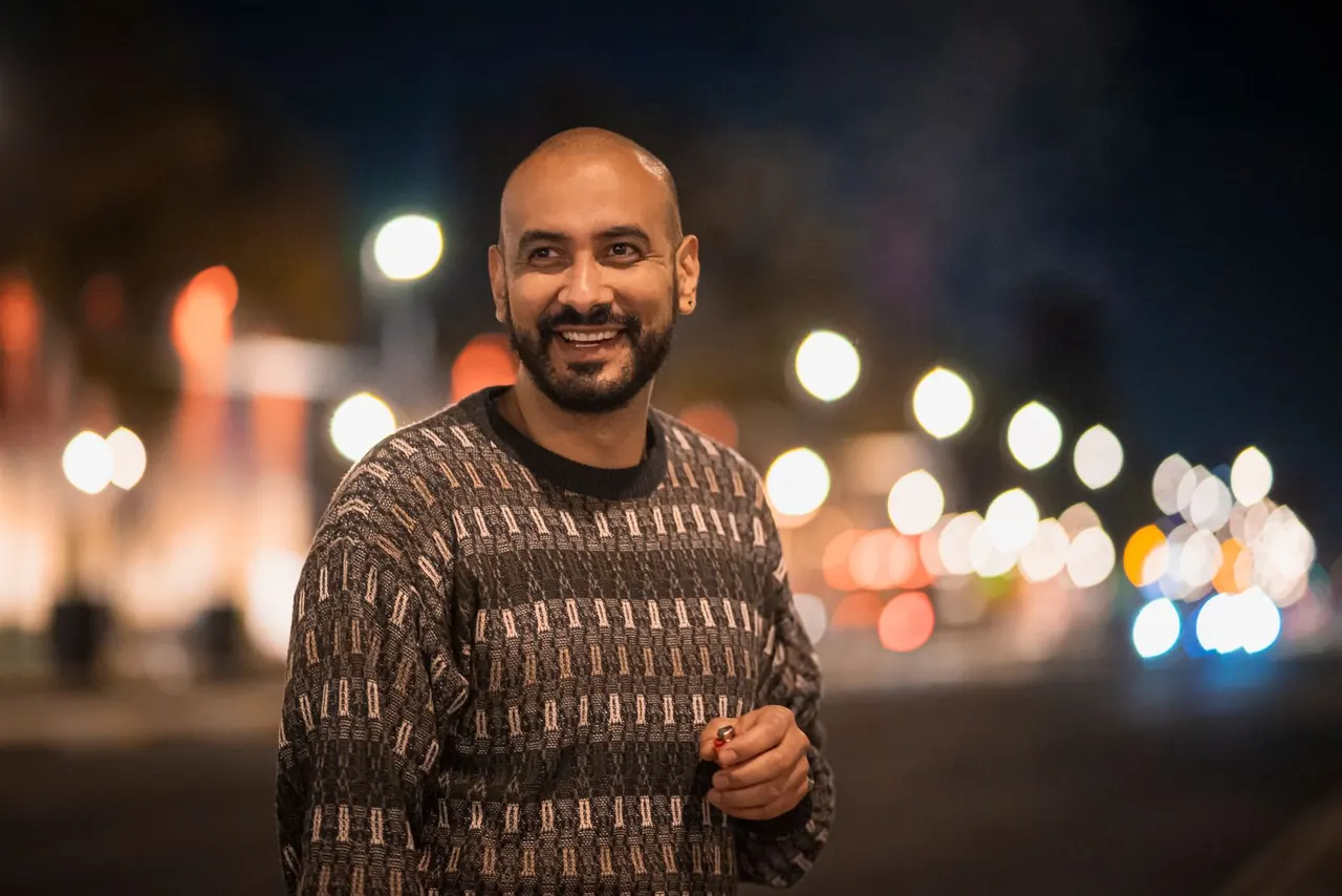 Hombre sonriendo en una avenida iluminada del centro de la ciudad, de noche.